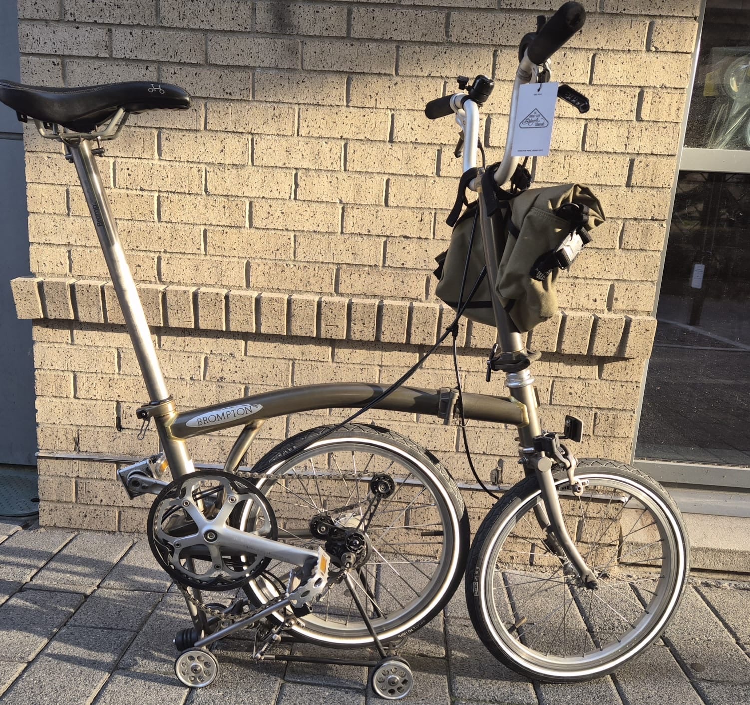 Foldable bicycle with a backpack attached against a brick wall.