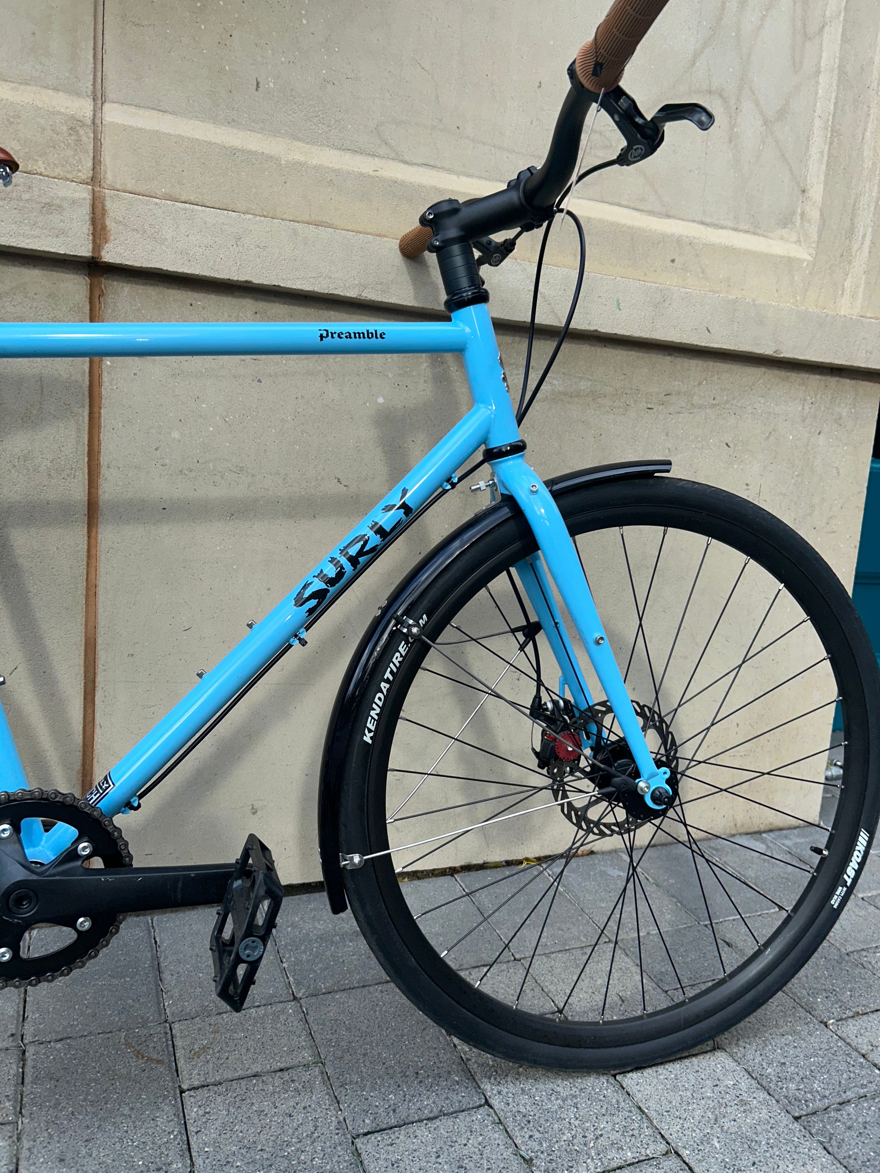 Blue bicycle with 'Surly' branding parked against a light-colored wall.