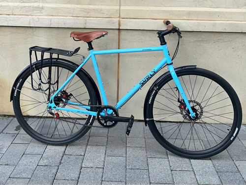 Blue bicycle parked on a sidewalk with a Christmas wreath hanging on a wall in the background.