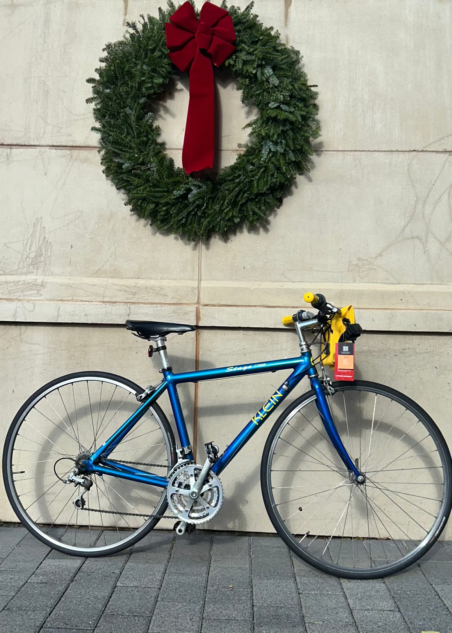 Blue bicycle leaning against a building with a Christmas wreath on a clear day.