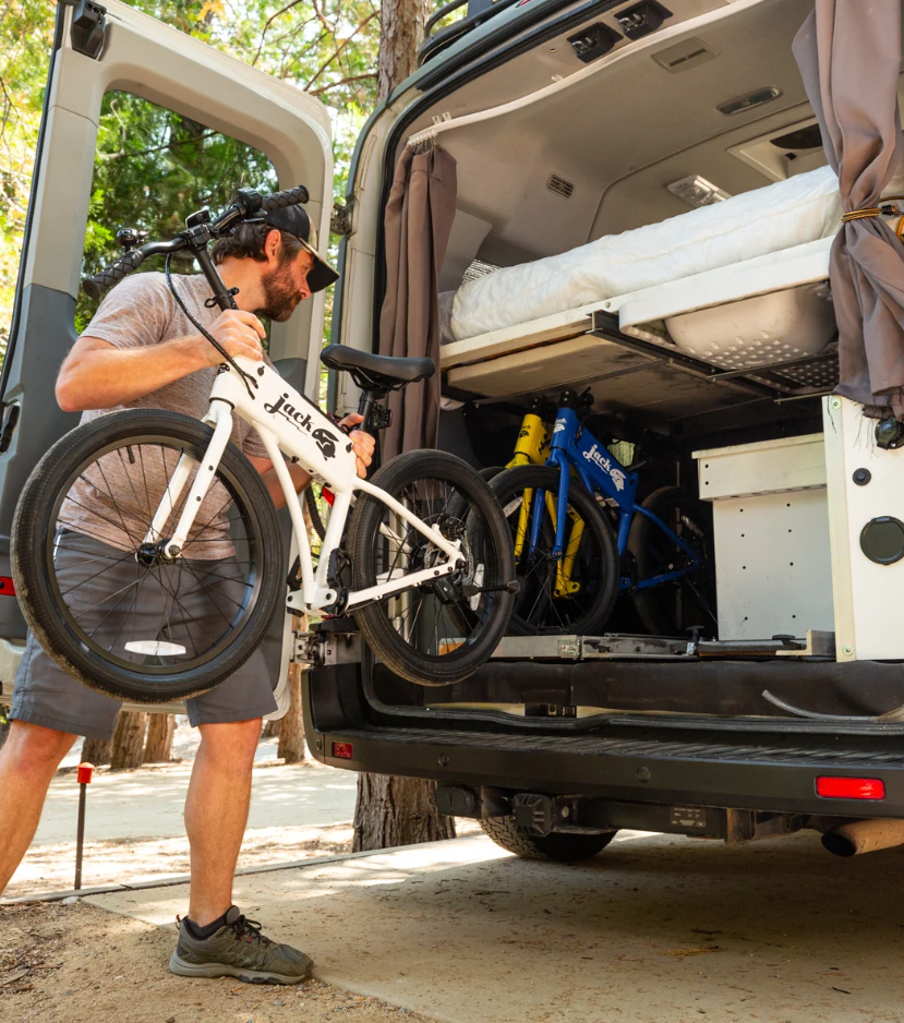 Man loading a bicycle into the back of a van with another bike already inside.