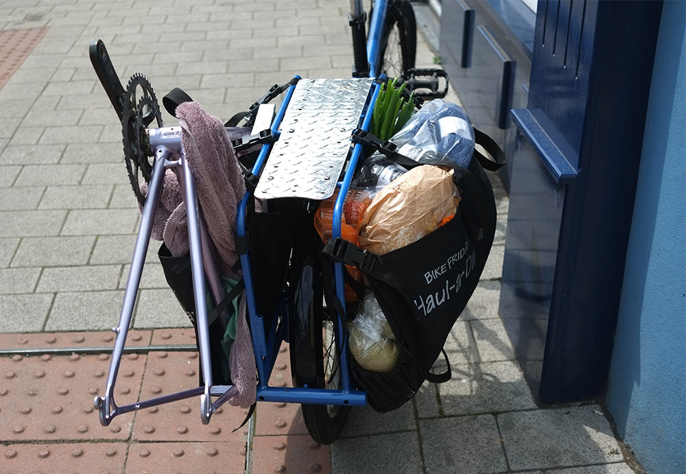 Blue bicycle with a basket full of groceries on a sidewalk.