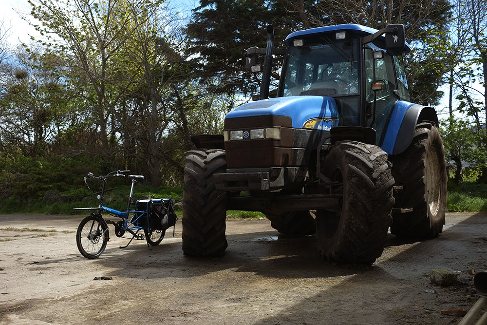 Large blue tractor and small bicycle on a dirt road with trees in the background