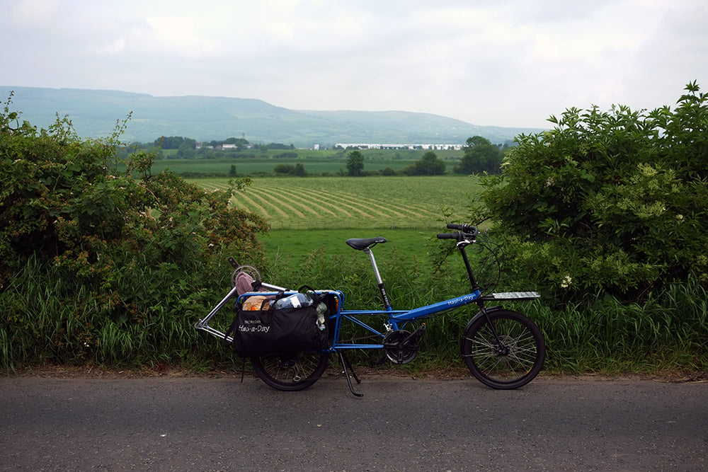 Blue tandem bicycle on a road with green fields and hills in the background