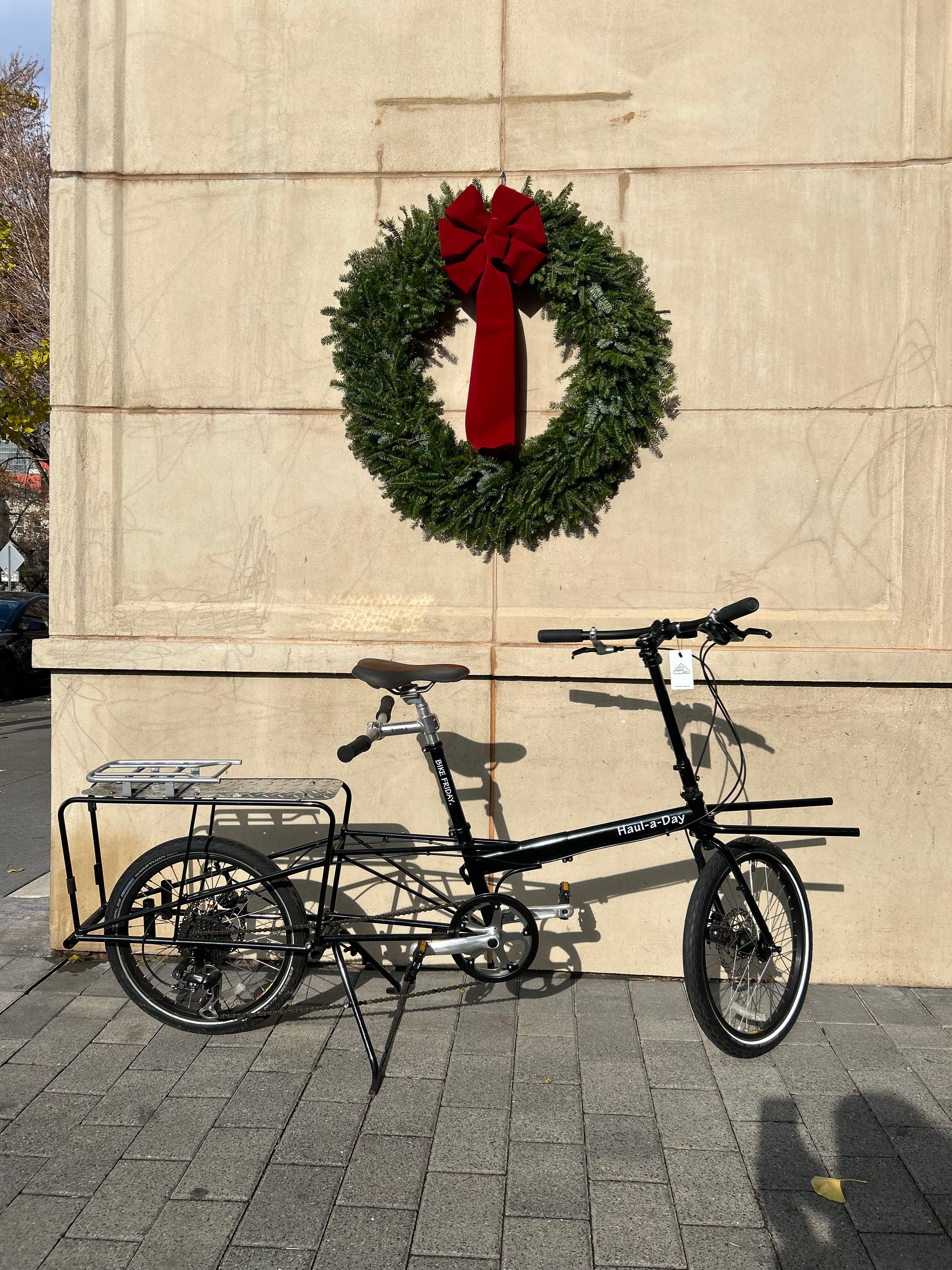 Bicycle with a trailer attached parked in front of a building with a Christmas wreath.