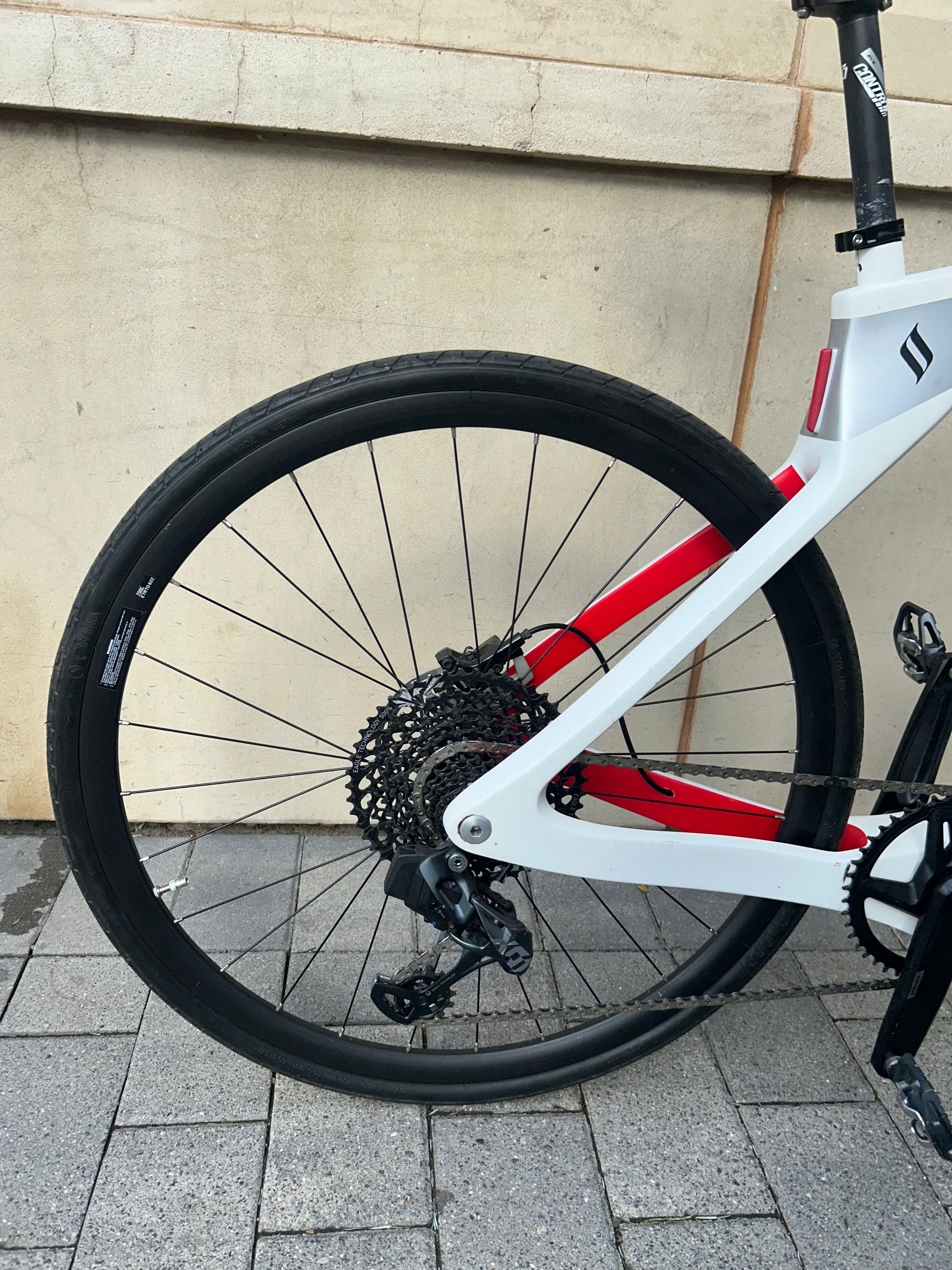 Bicycle wheel and frame with a red accent against a beige wall.