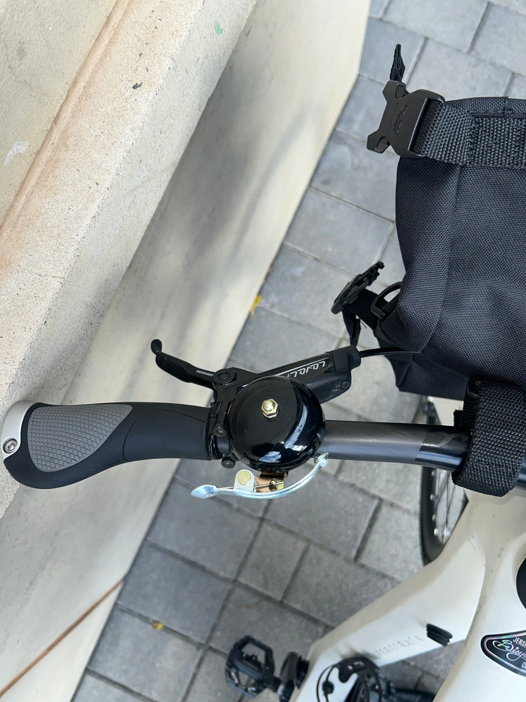 Close-up of a bicycle handlebar with a bell on a sidewalk.