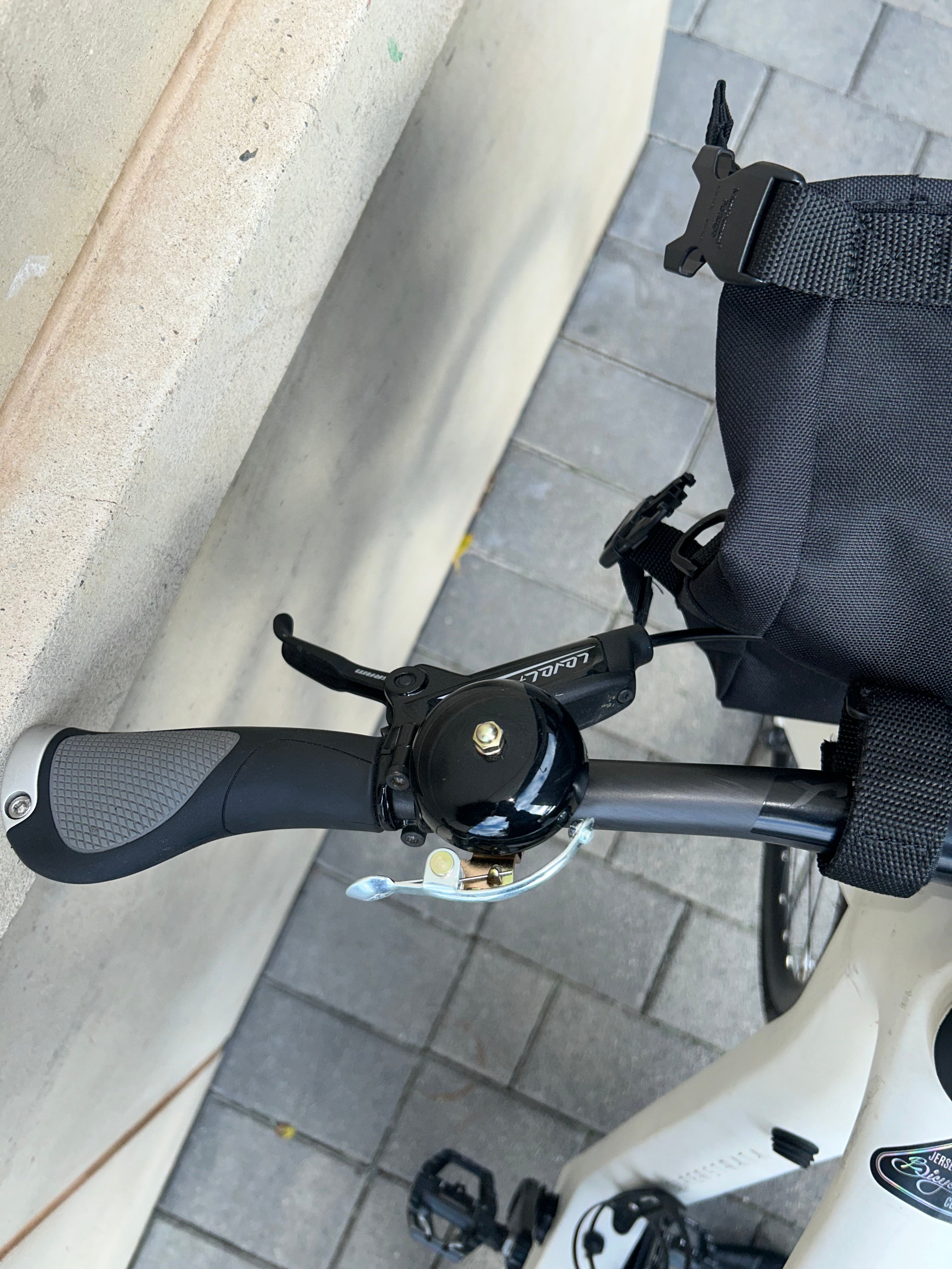 Close-up of a bicycle handlebar with a bell on a sidewalk.