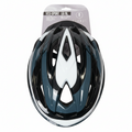 A black, white, and dark teal bicycle helmet in its original retail packaging, displayed flat on a light brown wooden floor. The packaging header card is visible at the top.