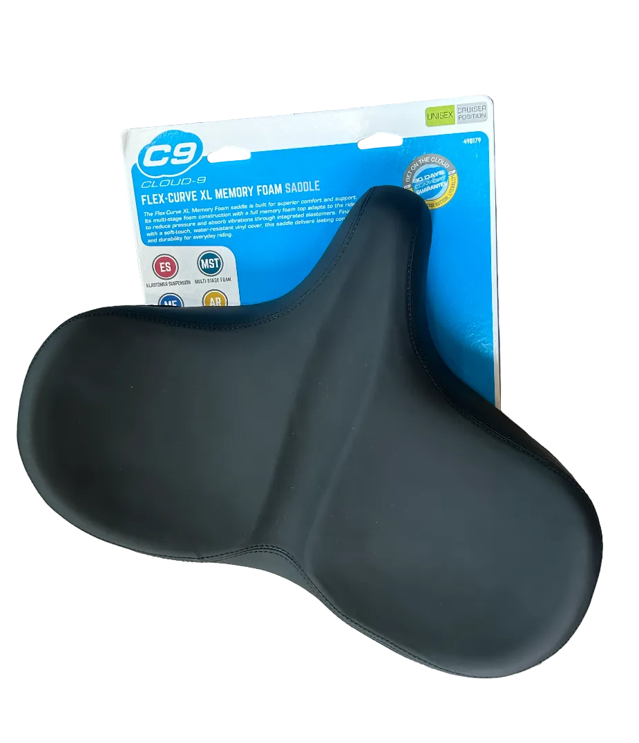 A black C9 Curves XL Memory Foam Saddle resting on its original retail packaging, placed on a gray wood plank floor.
